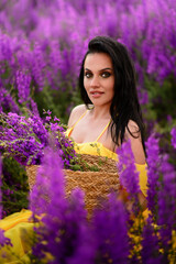 Beautiful young woman in a yellow dress sits in a field of purple flowers. Close up portrait.