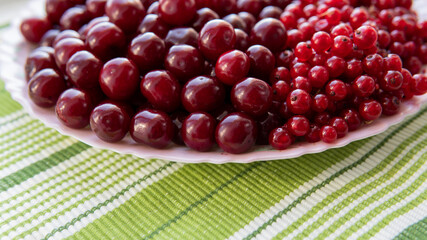 Healthy food concept. Ripe juicy cherries and red ribes on a plate. A bowl of organic fresh fruits on a green cloth. Vegetarian food.