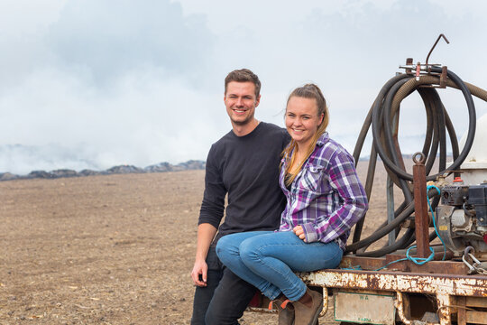 Happy young country couple sitting on back of old ute with smoke in background
