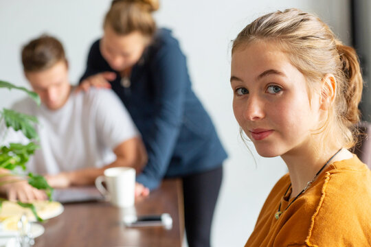 Young woman looking at camera with couple in background at table