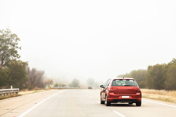 Red car overtaking in the right hand lane in foggy conditions