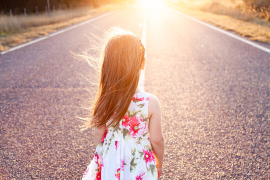 Little girl looking towards sunset along road