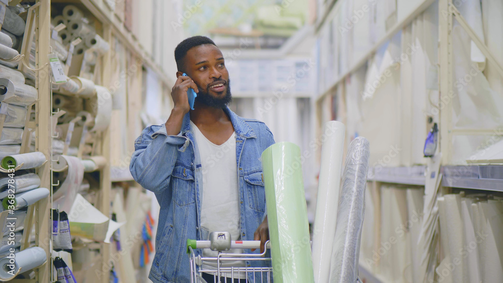 Wall mural african man talking on phone pushing trolley with wallpapers in diy store