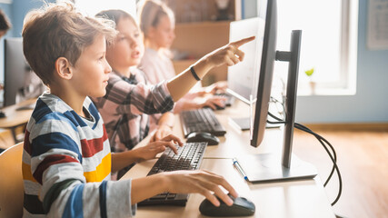 Elementary School Computer Science Classroom: Smart Girl Helps Boy Classmate with using Personal...