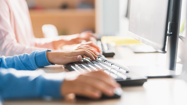 Close-up in School Computer Science Classroom: Smart Little Schoolchildren Working Personal Computers, Typing on Keyboards, Using Computer Mouse. Schoolchildren Getting Modern Education. Focus on Hand