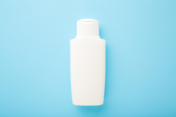 White plastic bottle on light blue table background. Pastel color. Care about face, hands, legs and body skin. Beauty product. Closeup. Empty place for text or logo. Top down view.