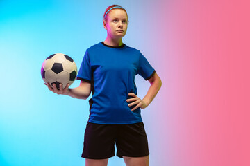 Confident posing. Female soccer, football player training in action isolated on gradient studio background in neon light. Concept of motion, action, ahievements, healthy lifestyle. Youth culture.