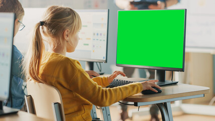 Elementary School Computer Science Classroom: Cute Little Girl Uses Green Mock-up Screen Computer...