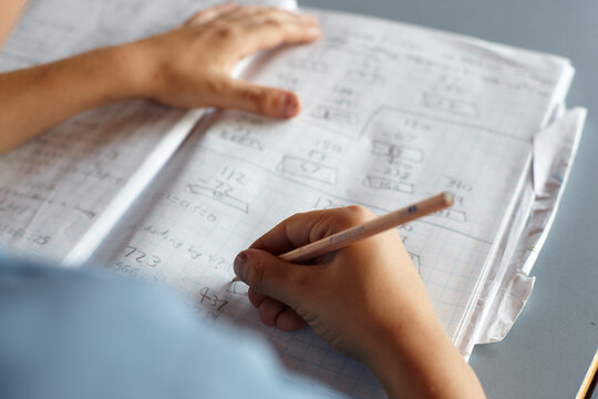 Young school boy doing maths in homework book in class