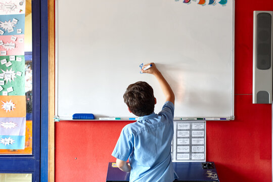 Young school boy at school writing on white board