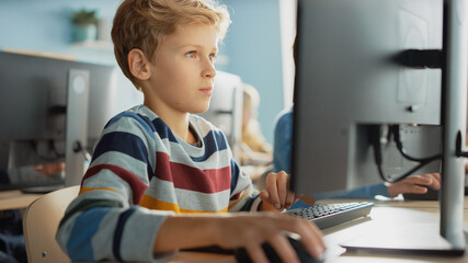 Elementary School Classroom: Smart Boy Uses Personal Computer, Learning How to Use Internet Safely,...