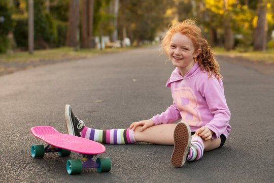 Girl sitting on a the street with a skateboard