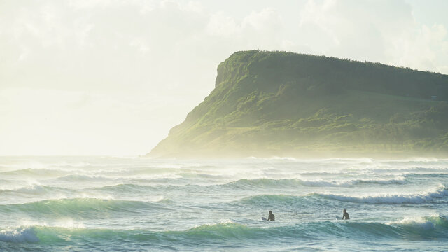 Men surfing in sea with Lennox Headland in background