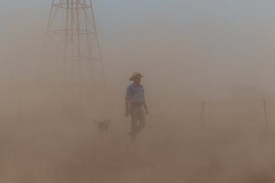 Farmer & working dog in the dust with windmill