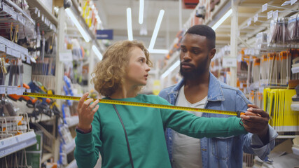 Fototapeta na wymiar Young multiethnic couple in hardware store using measuring tape