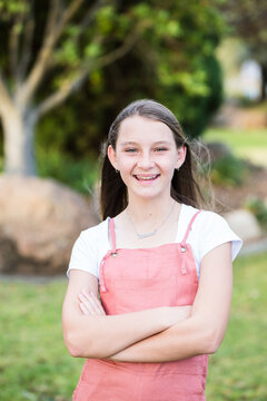 Young girl standing with arms crossed smiling in garden