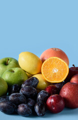 Mixed fruit in drops of water: plums, apples, lemons, grapefruit and a cut orange on a blue background. Vertical orientation, copy space