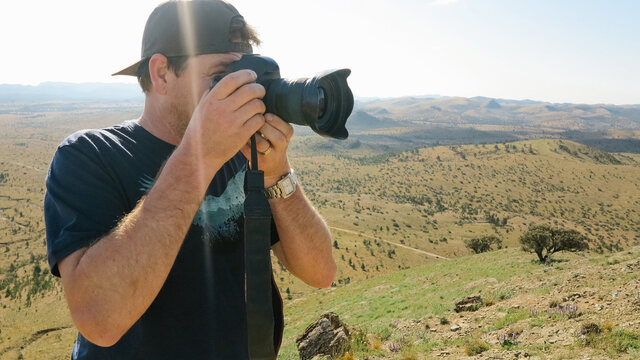 A man looking through the viewfinder of his camera with a vast landscape behind