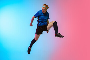 High jumping. Female soccer, football player training in action isolated on gradient studio background in neon light. Concept of motion, action, ahievements, healthy lifestyle. Youth culture.