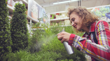 Fototapeta premium Woman gardener with sprayer watering plants in flower shop
