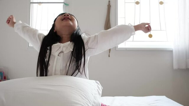 Asian child girl stretches after waking up in her bedroom