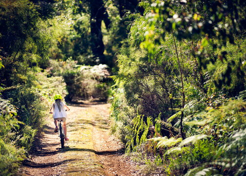 Girl riding a bike down a dirt road surrounded by dense bush