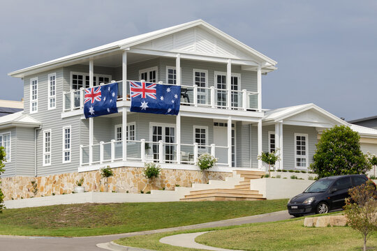 Grey and white Hamptons style house with two large Australian flags hanging from railings
