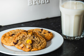 Three deliciously and freshly baked warm chocolate chip cookies with a cold glass of milk, ready to be eaten as yummy snack to enjoy at any time of the day.