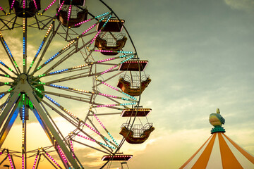 Colorful ferris wheel at sunset, illuminated by neon lights with a circus tent. Background with...