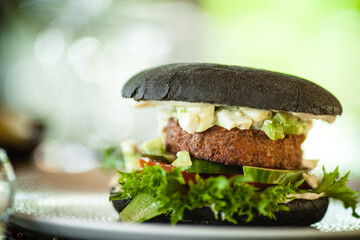 Vegan burger. Black bun, tofu-avocado salad, mayonnaise, cucumber, tomato, fresh salad. Delicious healthy hamburger food closeup served on a table for lunch in modern cuisine gourmet restaurant.