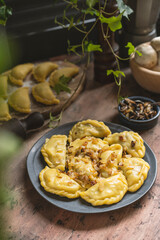 Homemade dumplings with potato and mushroom, blue plate, wooden rustic table at kitchen near window. Organic, healthy vegetable vegan food. Selective focus, copy space. 