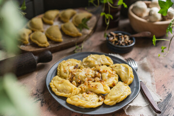 Homemade dumplings with potato and mushroom, blue plate, wooden rustic table at kitchen near window. Organic, healthy vegetable vegan food. Selective focus, copy space. 