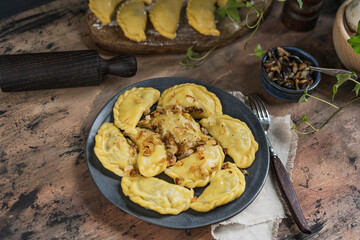 Homemade dumplings with potato and mushroom, blue plate, wooden rustic table at kitchen near window. Organic, healthy vegetable vegan food. Selective focus, copy space. 