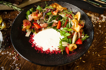 Crudo ham salad. Stracciatella and Grana Padano cheese, sundried tomato, fresh cucumber. Delicious healthy mixed greens food closeup served on a table for lunch in modern cuisine gourmet restaurant.