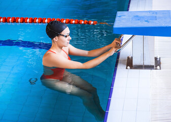 Young woman swimmer in a swimsuit getting ready to start swimming in a swimming pool. Professional...