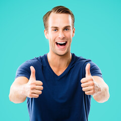 Portrait of happy smiling man in casual clothing, showing thumb up gesture, against aqua marine blue color background. Male caucasian model at studio. Copyspace area for some ad sign text.