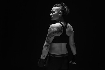 A young, female boxer with dark hair styled with a fade on one side, stands in contemplation of her next bout. 