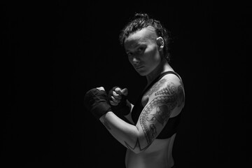 A young, female boxer with dark hair styled with a fade on one side, stands in contemplation of her next bout. 