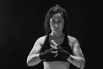 A young, female boxer with dark hair styled with a fade on one side, stands in contemplation of her next bout. 