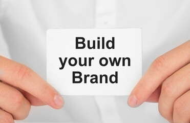 Man's hands take a card with words Build your own brand, finance and business concept.