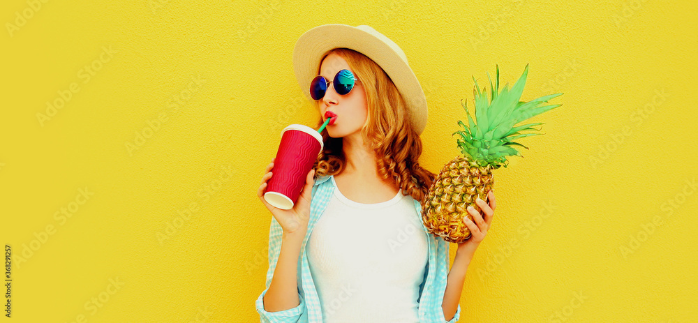 Wall mural summer portrait of attractive woman drinking juice holding pineapple wearing a straw hat, sunglasses