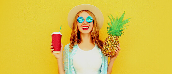 Summer portrait of happy laughing woman with cup of juice and pineapple having fun wearing a straw hat, sunglasses over colorful yellow background