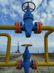 Pipeline fittings and manifold of producing gas wells in the field. Handwheels for high pressure valves. In the background, a drilling rig. Blurring distant objects.