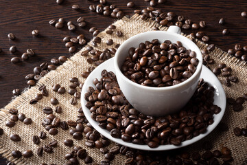 Roasted coffee beans in a white Cup on a wooden table. Coffee beans on burlap.