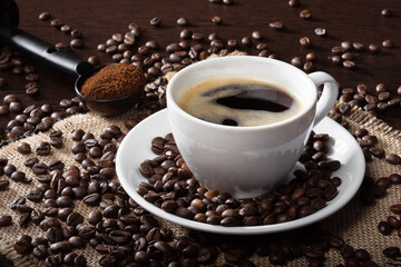 Roasted coffee beans on a wooden table. Coffee beans on burlap. Fresh brewed coffee in a mug. Ground coffee for the Express car in a measuring spoon.