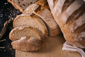 Assortment of baked bread and bread rolls on black table black background.