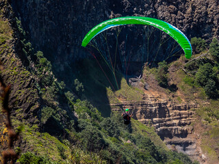 Para glider soars over the beach, waves and hills at Murawai Beach, Auckland, New Zealand