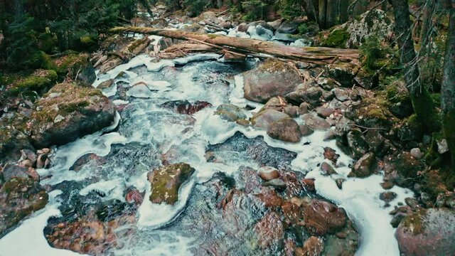 mountain river with ice with waterfalls in a green forest in winter, flight