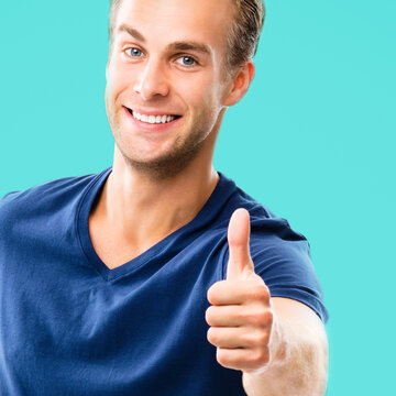 Portrait of happy smiling man in casual clothing, showing thumb up gesture, over aqua marine blue color background. Male caucasian model at studio picture. Square composition.
