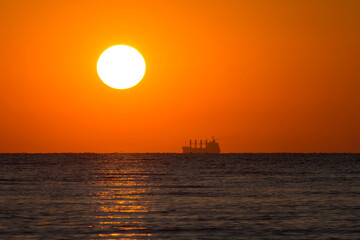Beautiful ocean sunrise, cargo container ship on the horizon. The sun rose over the horizon. The sky is orange.
